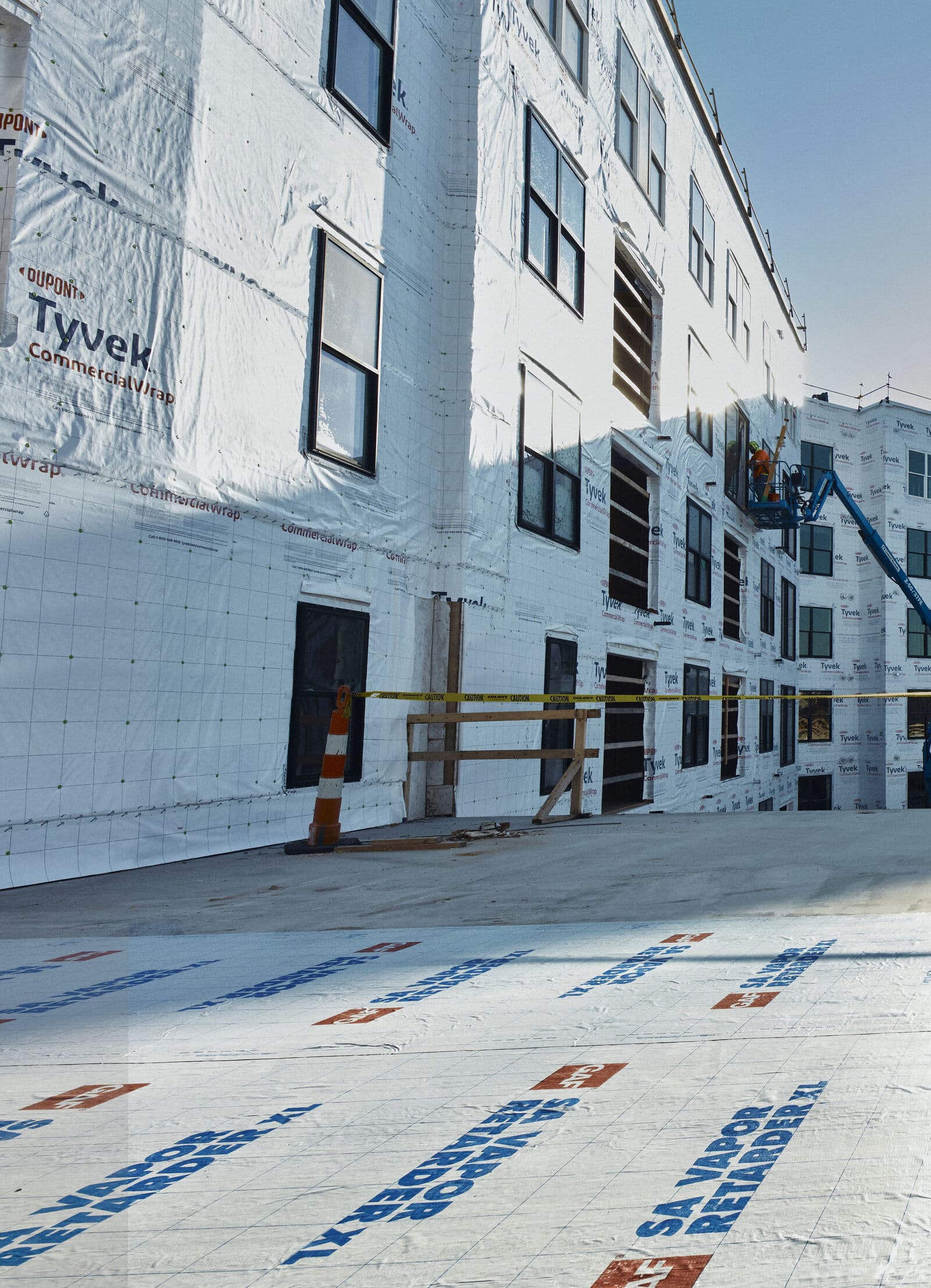 Multi-story commercial building wrapped for new exterior work, boom lift at the facade